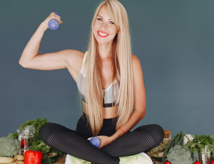 Woman lifting a small dumbbell while surrounded by fresh vegetables, embodying health and fitness.